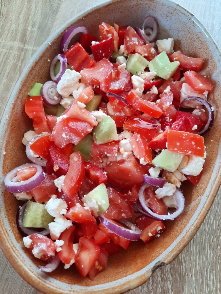 Braune Schale mit Griechischer Salat mit Feta, Tomaten, Gurken, Paprika und Zwiebeln.

