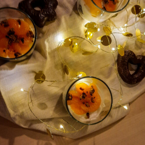 Drei Gläser mit dem Lebkuchen Tiramisu auf einem Tuch. Beleuchtet durch eine Lichterkette und Lebkuchen im Hintergrund.