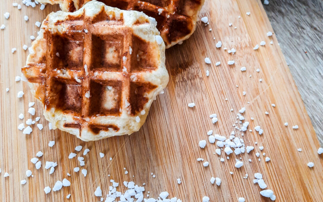 drei kleine Lütticher Waffeln mit Hefeteig auf einem Holzbrett. Um die Lütticher Waffeln ist Hagelzucker gestreut.