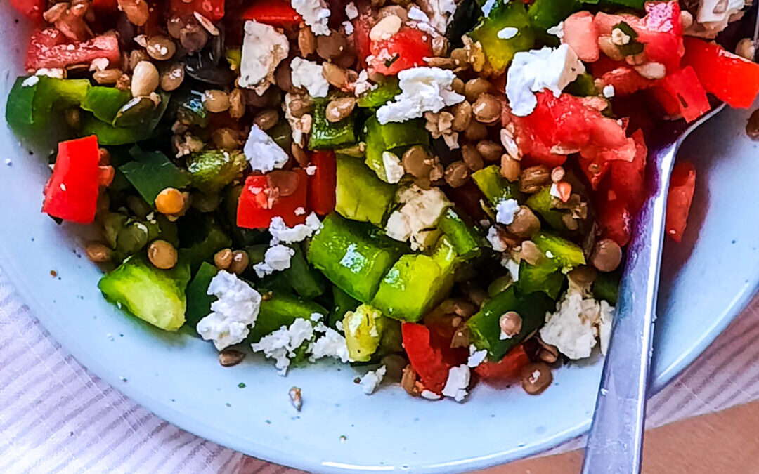 ein Teller mit Linsensalat mit Feta und Tomate. Zudem sindnoch Gurken und Paprika auf dem Bild zu sehen