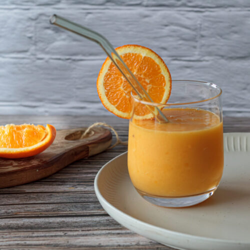zwei Gläser mit einfachem Orangen Smoothie, gerniert mit einer Orange und im Hintergrund liegen geschälte Orangenstücke.