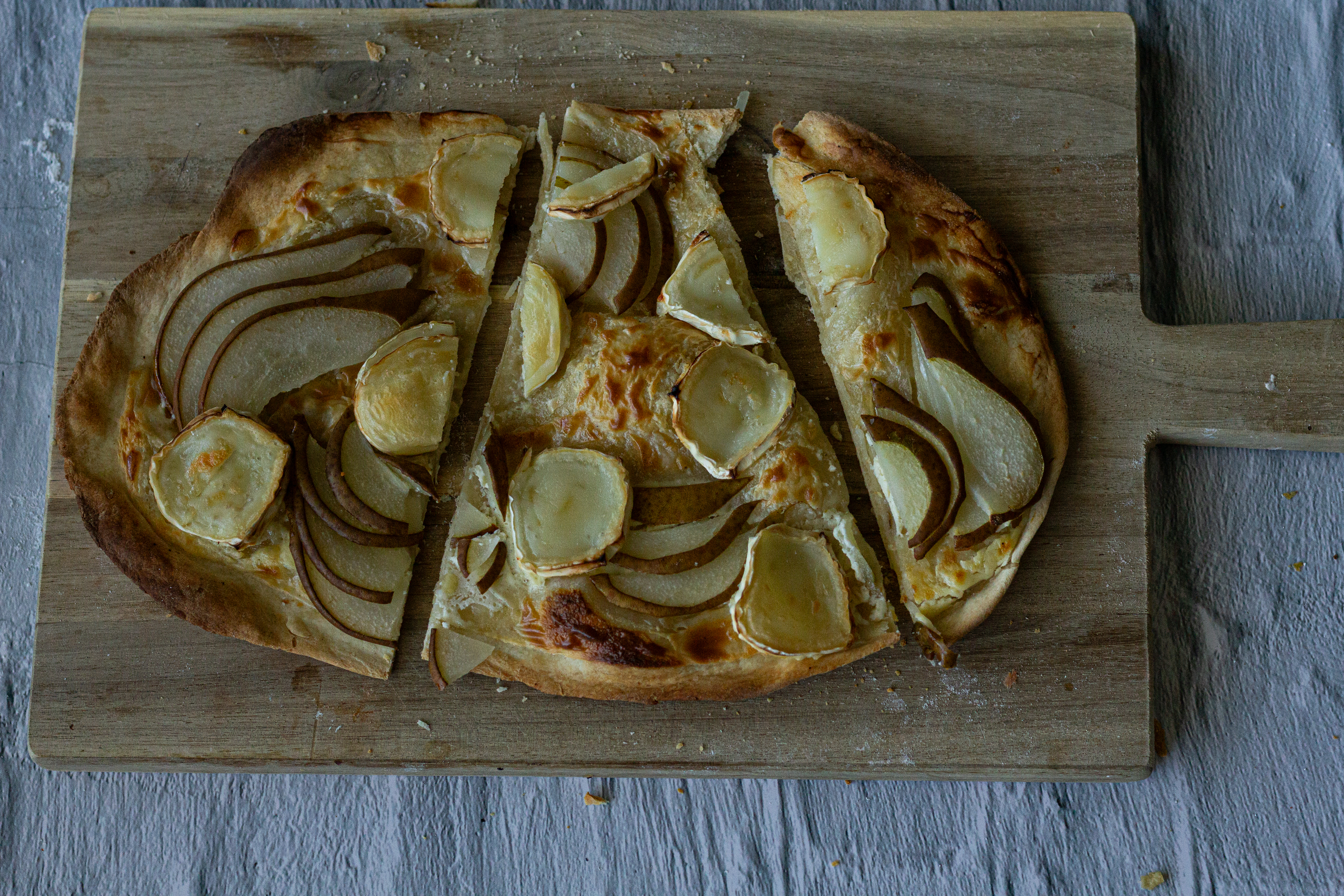 Flammkuchen mit Birne und Ziegenkäse in Stücke geschnitten auf einem Brett.